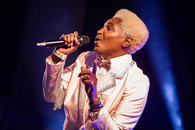 Don One wearing a pink suit singing into a microphone